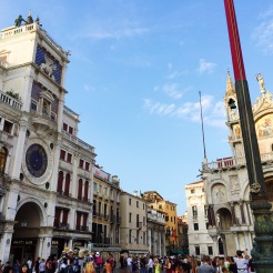 7. On the left is the Torre dell’Orologio (The Clock Tower), which was constructed in the fifteenth century. The most prominent feature is the blue-and-gold clock face which indicates the hour of the day, displayed in Roman numerals. On the right is the Bascilica di San Marco, which is known for its domes and mosaic decorations.